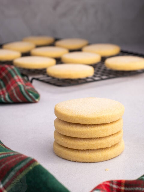 Stack of round Scottish shortbread biscuits with more cooling on a wire rack.