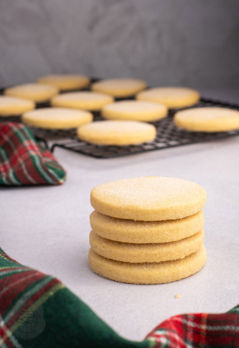 Stack of round Scottish Shortbread biscuits beside more biscuits on a wire cooling rack.