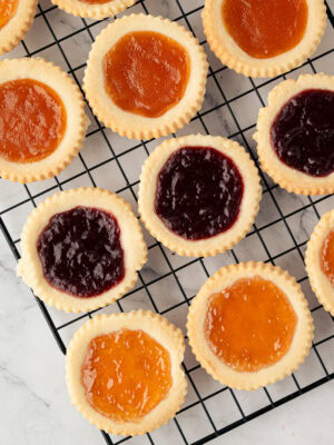 Freshly baked jam tarts with raspberry and apricot filling cooling on a wire rack