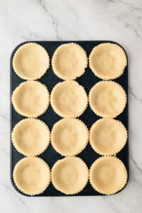 Shortcrust pastry cases in a baking tray prepared for making homemade jam tarts