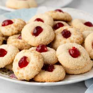 Plate of Melting Moments coated in oats and coconut and topped with glacé cherries.