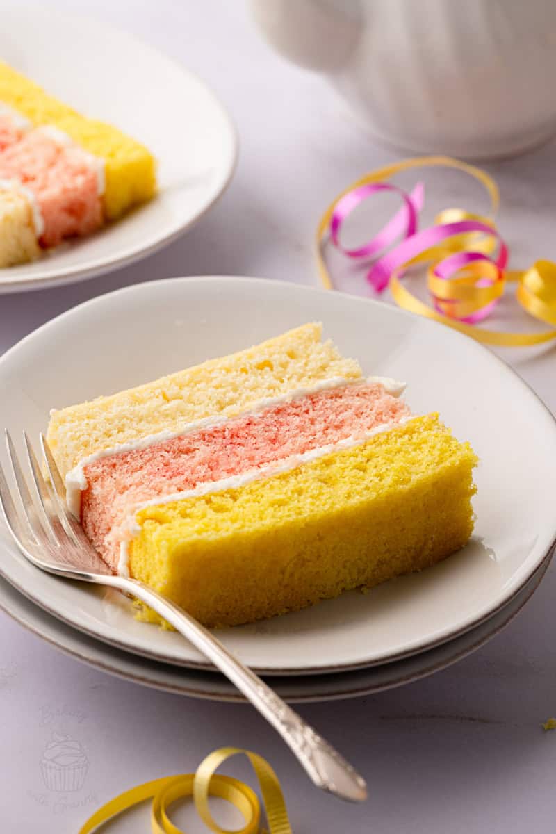 Slice of traditional British Angel Cake with three colourful sponge layers and buttercream filling.
