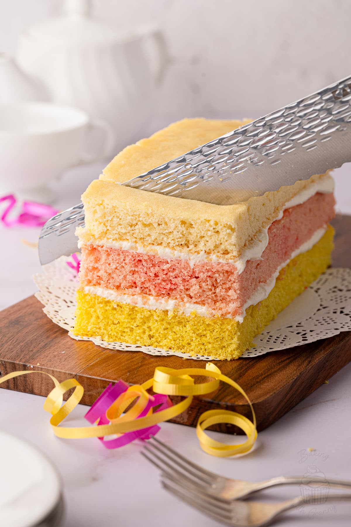 Angel Cake being sliced to reveal its colourful sponge layers and buttercream filling.