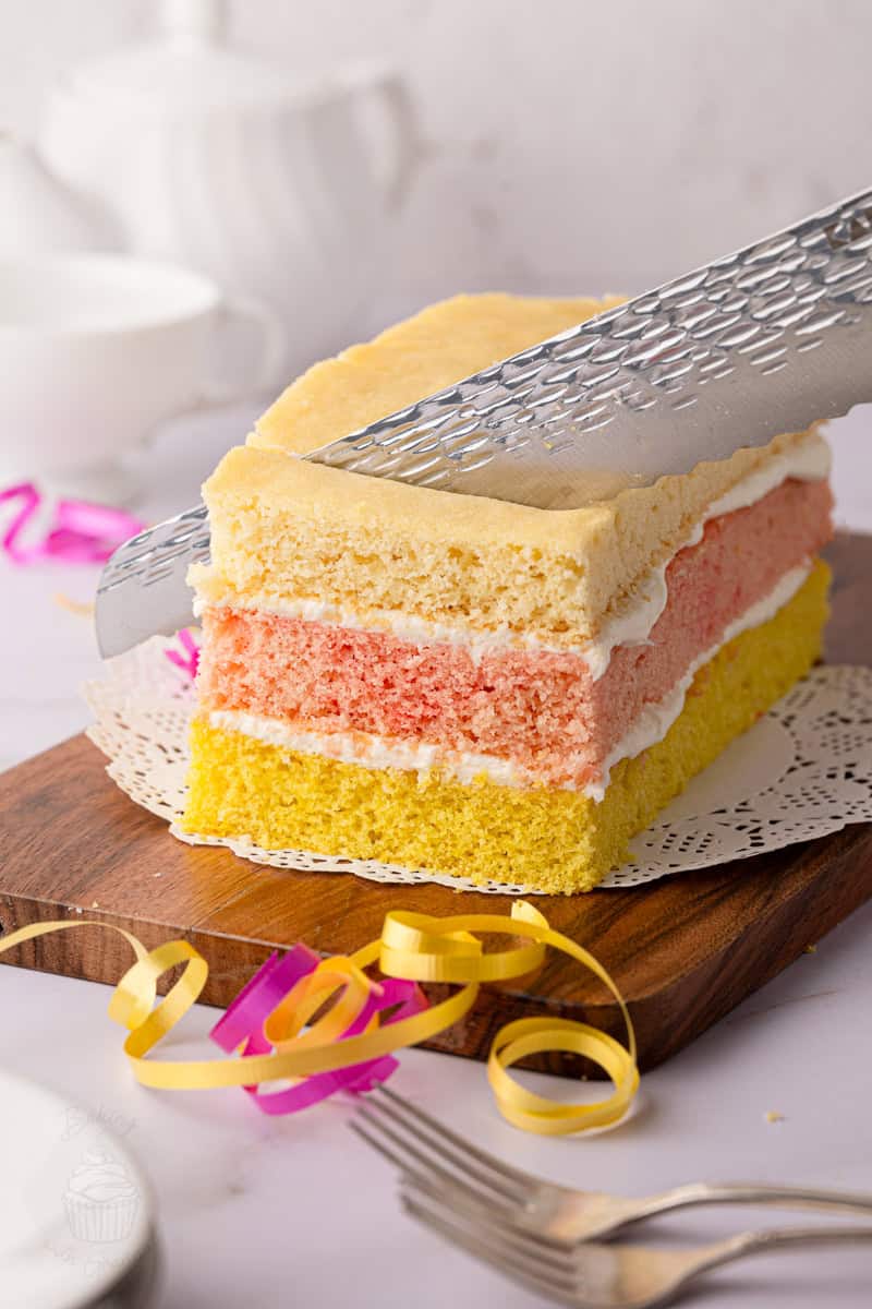 British Angel Cake being sliced to reveal its colourful sponge layers and buttercream filling.