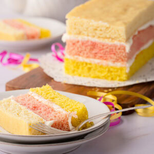 Angel Cake on a wooden board with a slice served in the background.