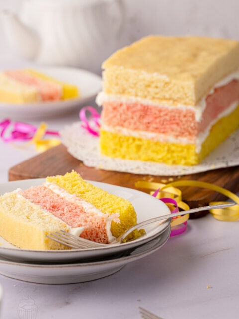 Traditional British Angel Cake on a wooden board with a slice served in the background.