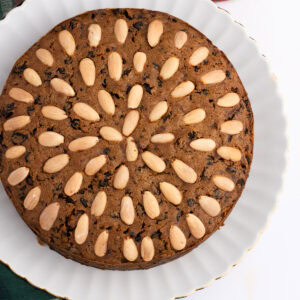 Traditional Scottish Dundee Cake, with almond topping, packed with rich dried fruit. On a white plate, atop a tartan fabric.