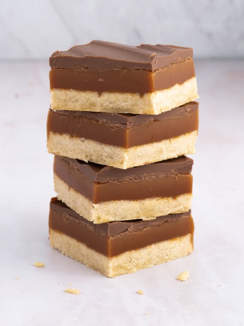 Tower of Scottish Caramel Slice with neat layers of shortbread, golden caramel, and chocolate, on a light background.