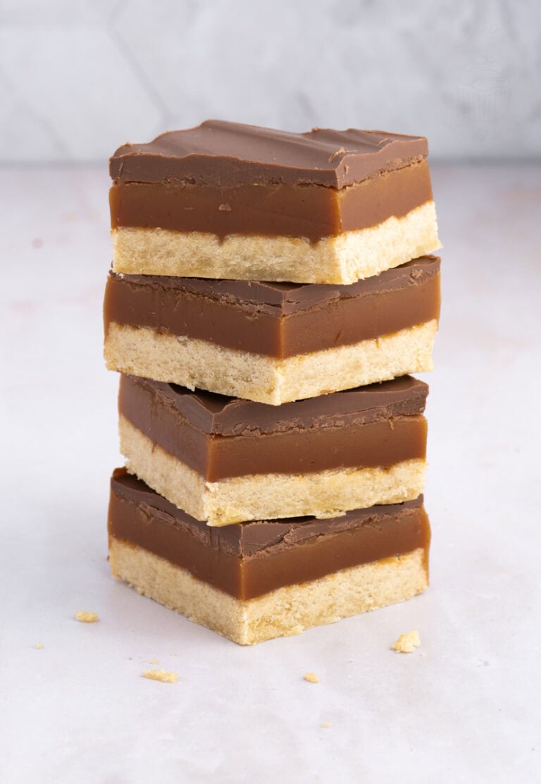 Tower of Scottish Caramel Slice with neat layers of shortbread, golden caramel, and chocolate, on a light background.