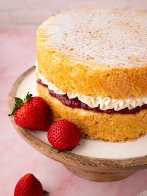 Victoria Sponge filled with strawberry jam and piped buttercream, with fresh strawberries alongside.