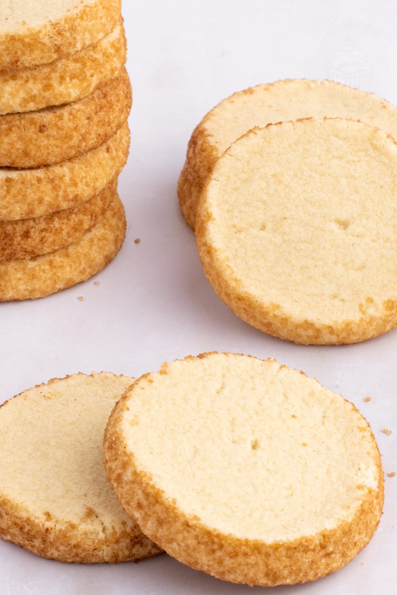 Round Highlander Shortbread biscuits coated with golden sugar, some stacked and some lying flat on a white surface