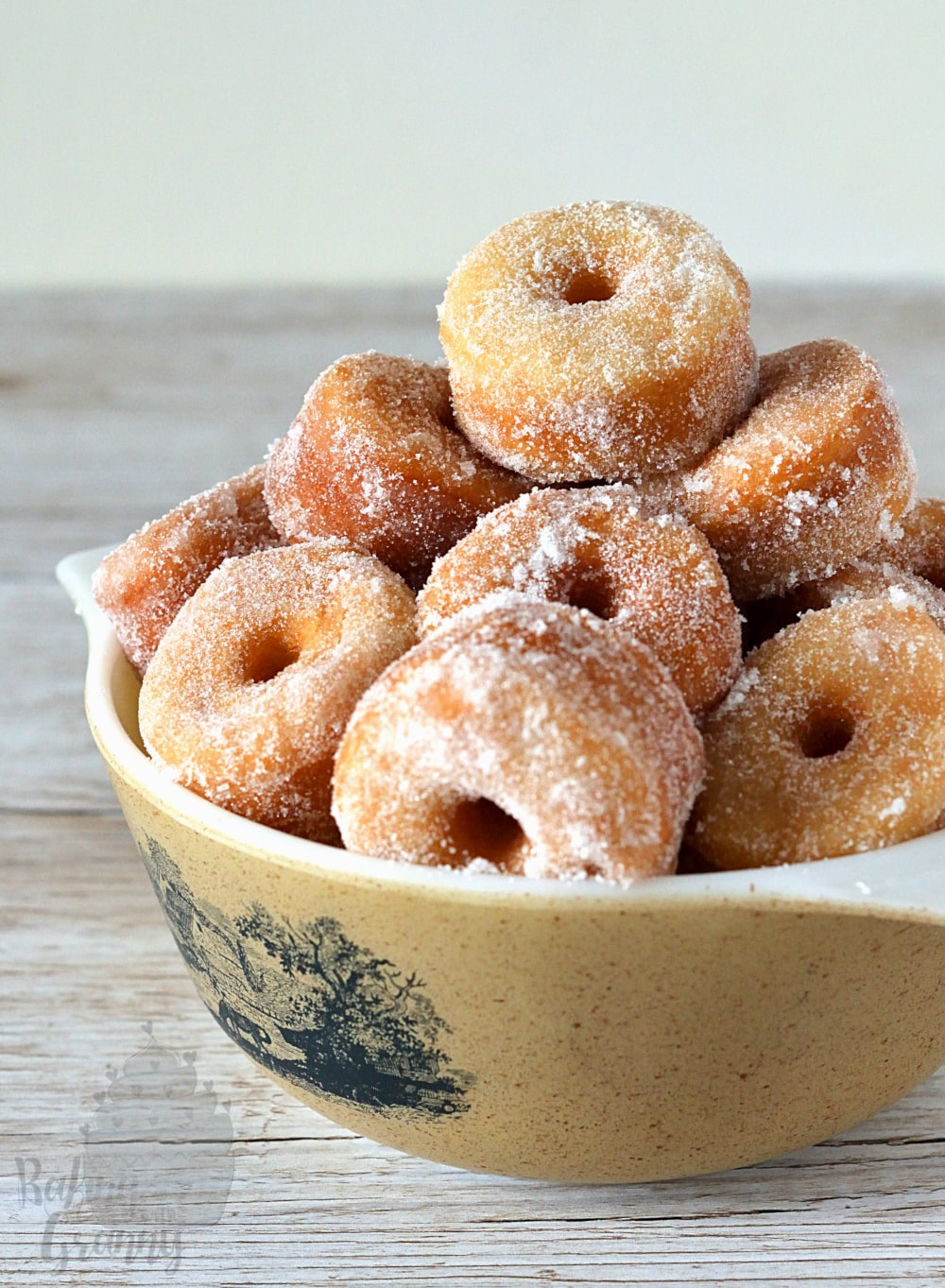 Bowl full of mini ring donuts, covered in sugar.