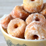Bowl full of mini ring doughnuts, covered in sugar.