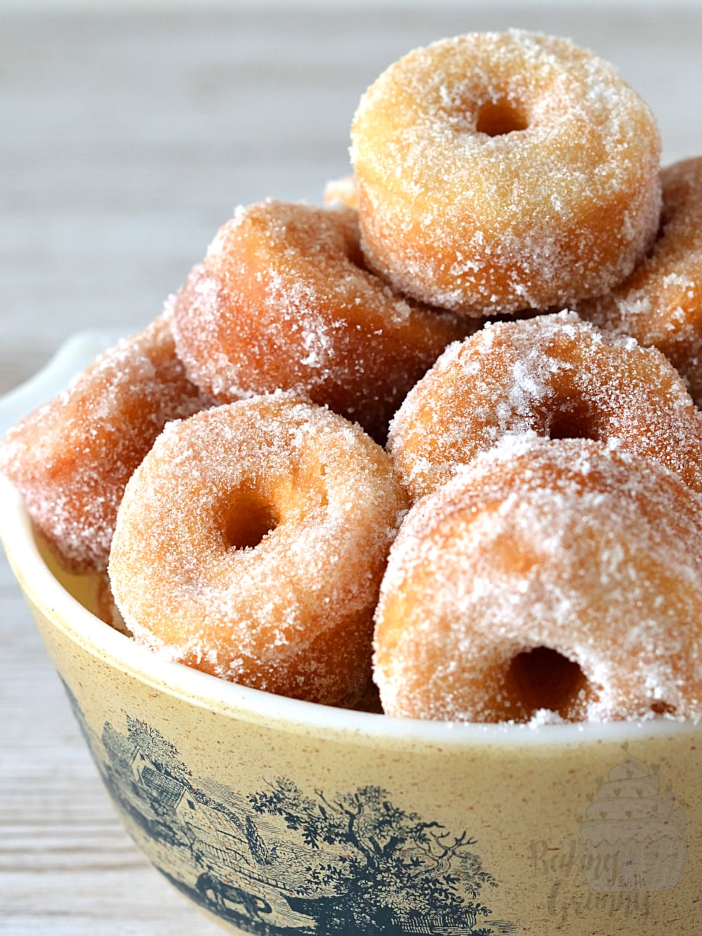 Bowl full of mini ring doughnuts, covered in sugar.