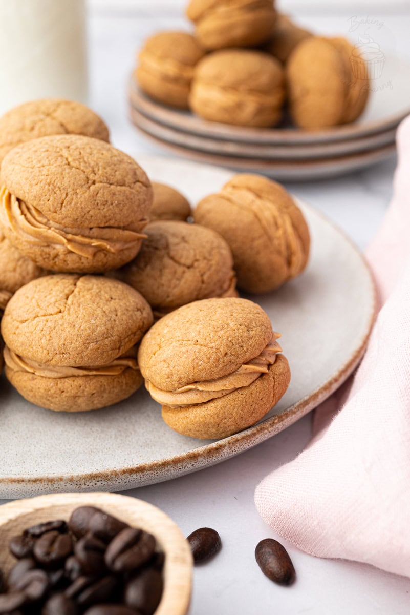 Finished coffee kisses biscuits stacked on a plate, showing the coffee buttercream filling.