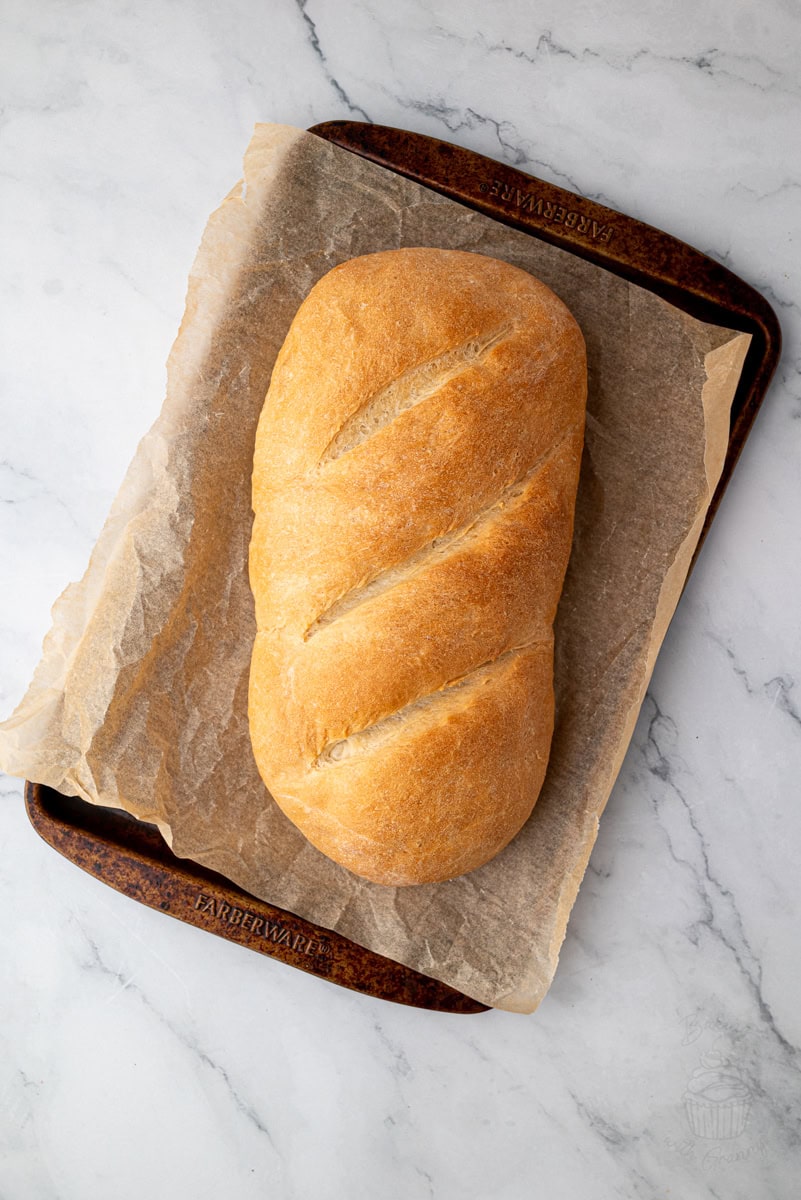 Homemade white bread loaf on a lined baking tray, viewed from above.