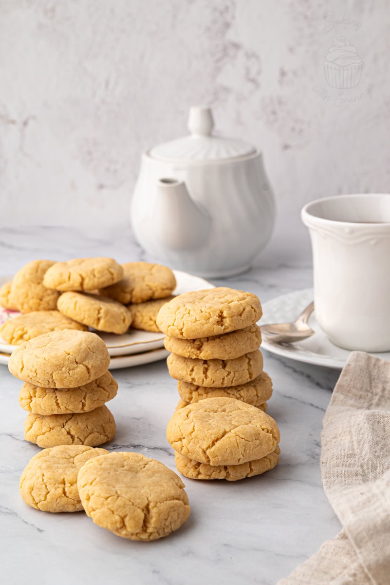 Stack of gingernut biscuits with a teapot and cups in the background.