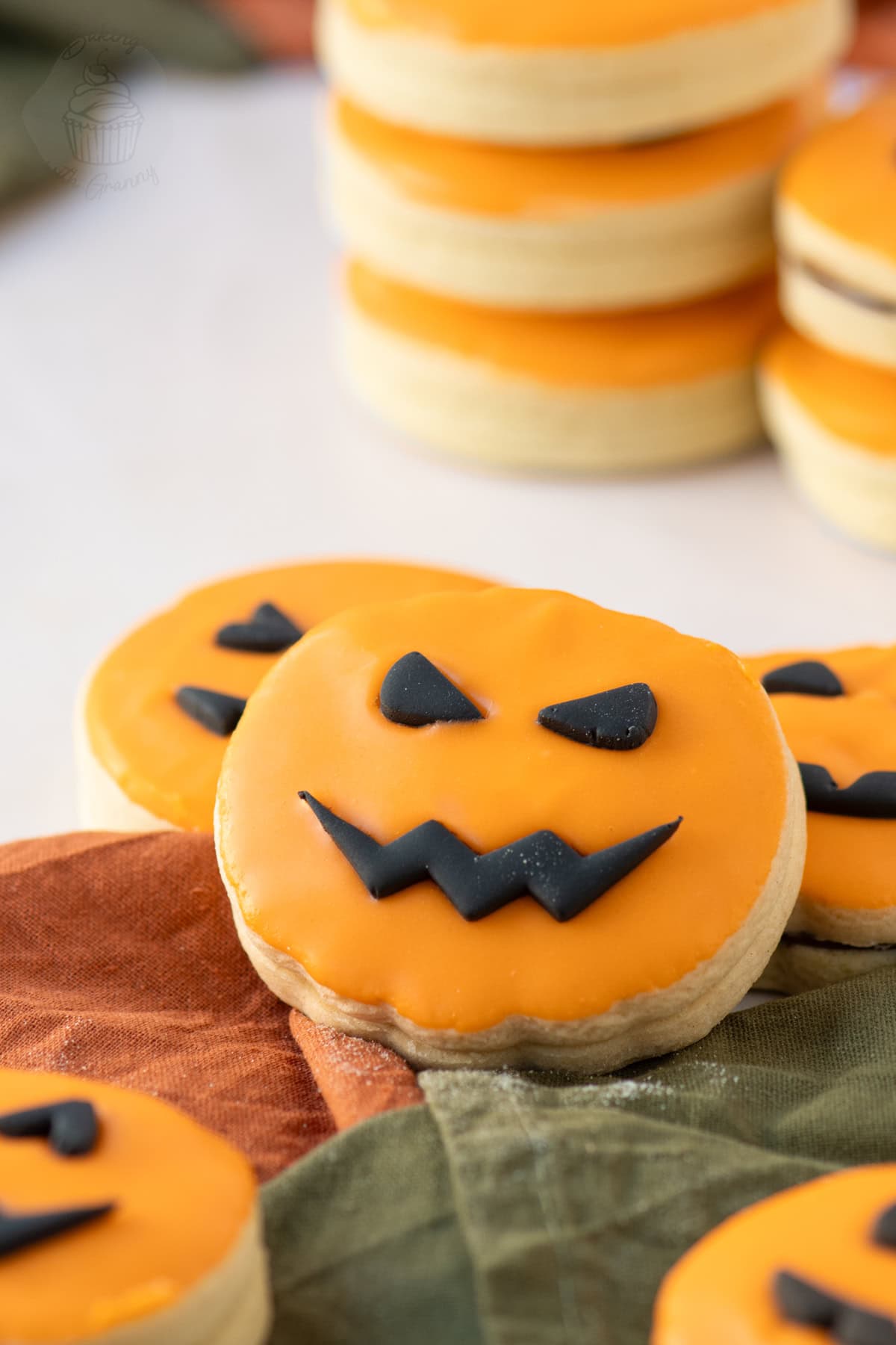 Close-up of an orange-iced Pumpkin Empire Biscuit with a black fondant pumpkin face.
