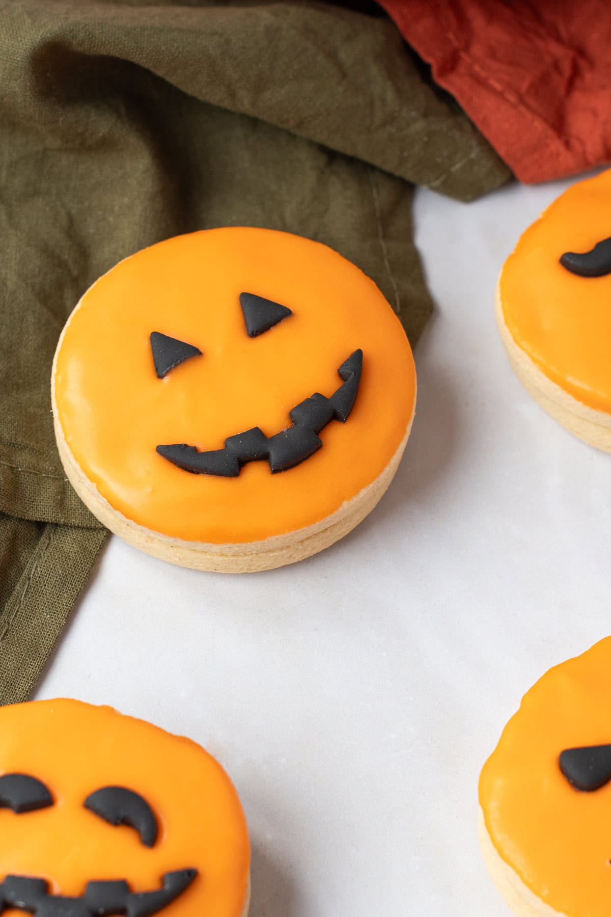 Several orange-iced Pumpkin Empire Biscuits with black fondant pumpkin faces arranged on a white background.