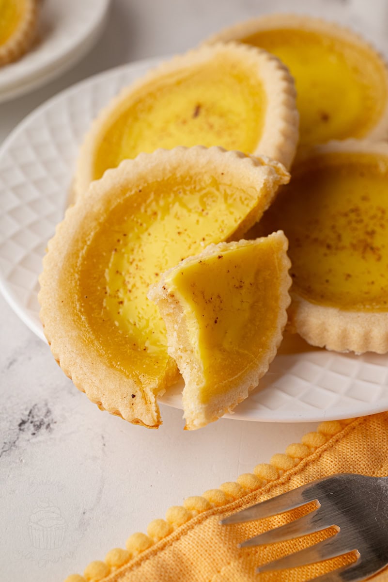 Detailed view of a sliced custard tart on a plate, showing smooth custard filling and shortcrust base.
