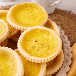 Plate stacked with traditional British custard tarts, served with a cup of tea in the background.
