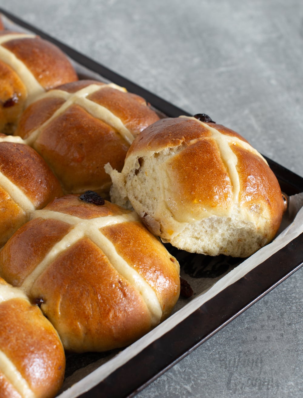 Close up of traditional hot cross bun showing soft fluffy crumb and dried fruit.