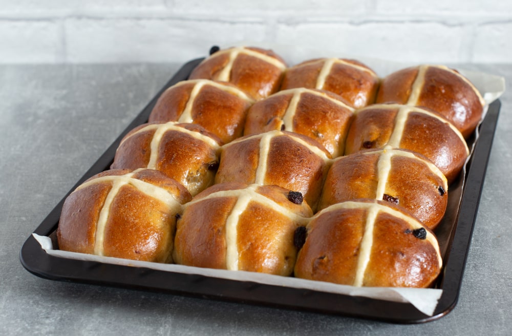 Traditional Easter hot cross buns in baking tray with golden glaze and dried fruit.