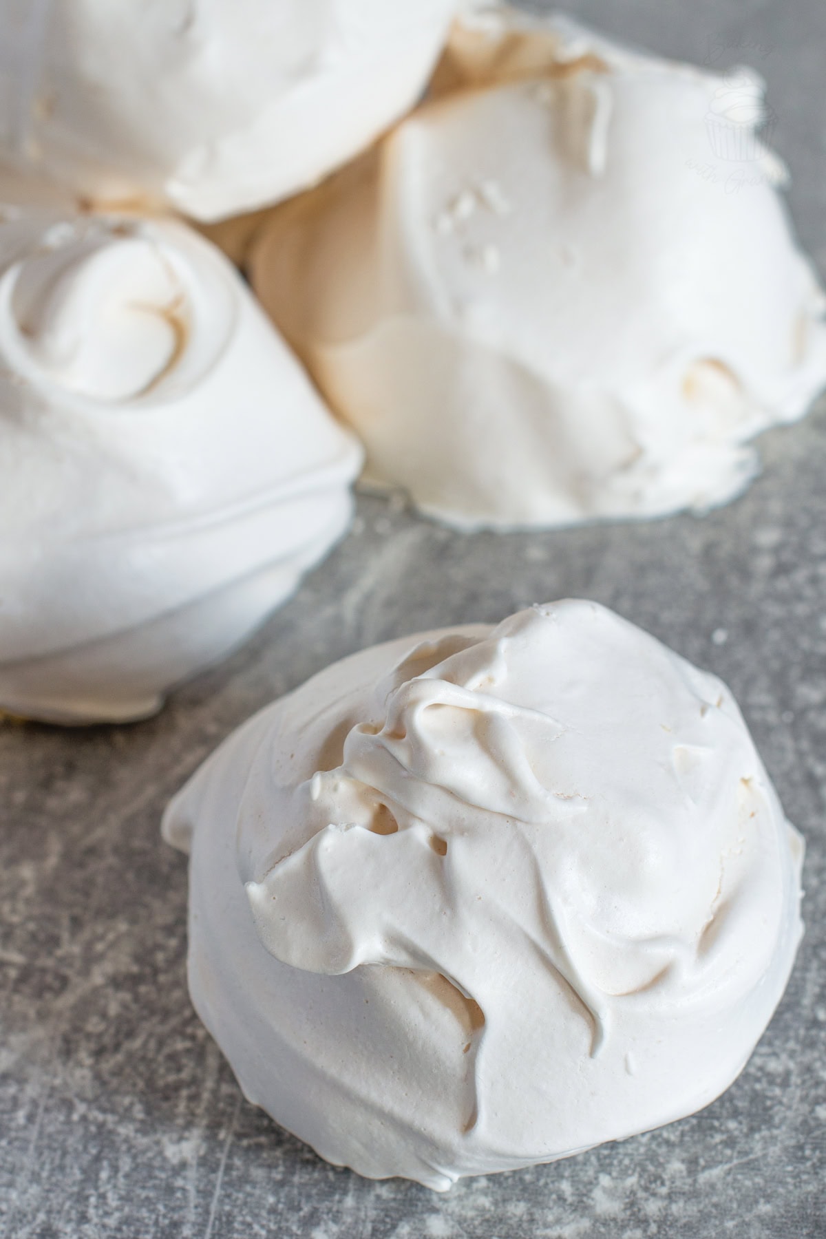 Homemade meringue with glossy peaks and a crisp white shell, photographed on a grey background.