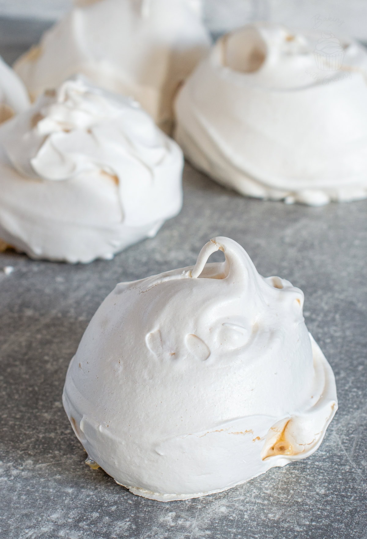 Large homemade meringue with a crisp white shell and glossy peak, styled on a cool grey surface.