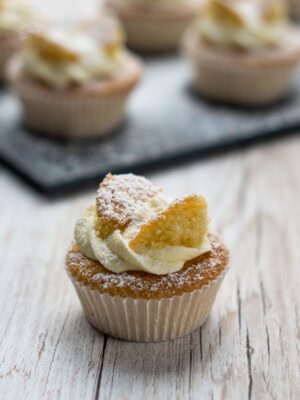 Individual butterfly cake with buttercream and sponge wings, with more cakes softly blurred in the background.