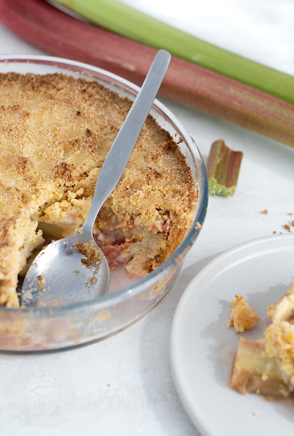 Easy Rhubarb Crumble in a glass baking dish with a spoon, showing the soft rhubarb filling and crumb topping.