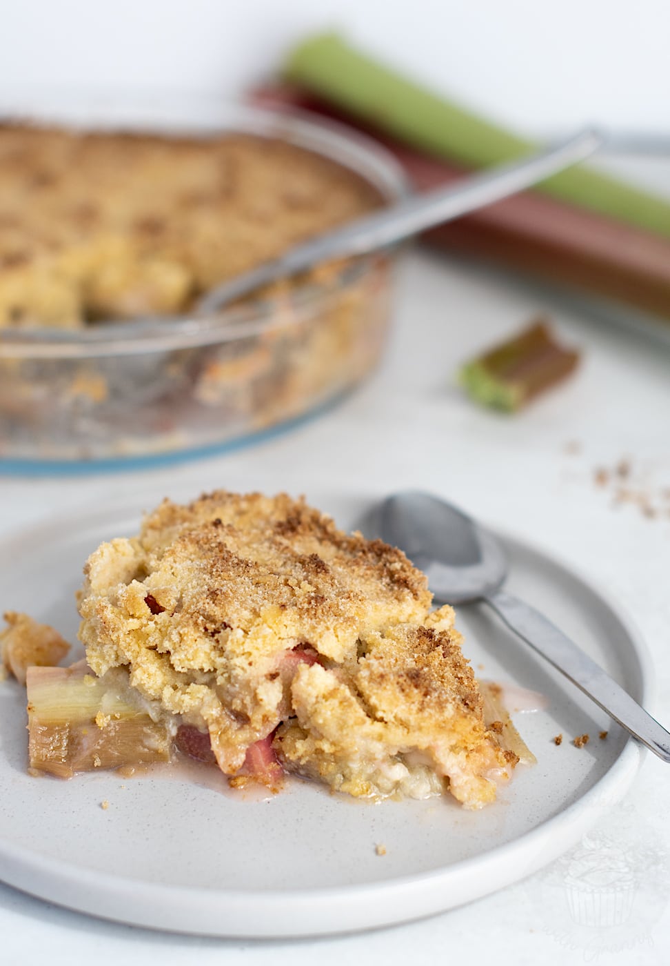 Serving of homemade rhubarb crumble on a plate, showing chunks of rhubarb and a golden, crumbly topping.