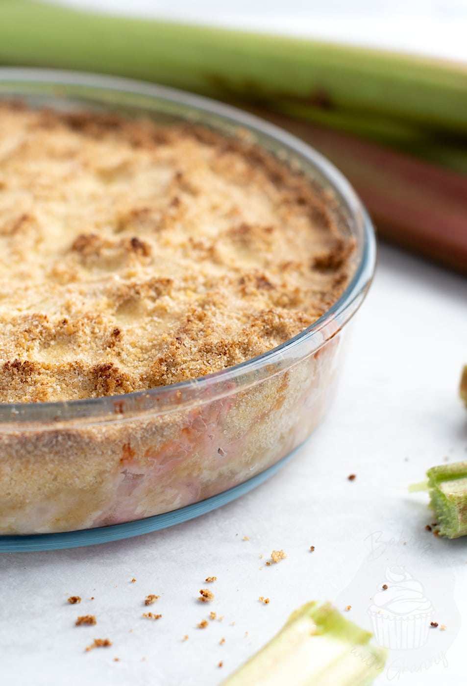 Side view of home cooked Rhubarb Crumble in a glass dish, showing layers of soft fruit and golden crumble topping.