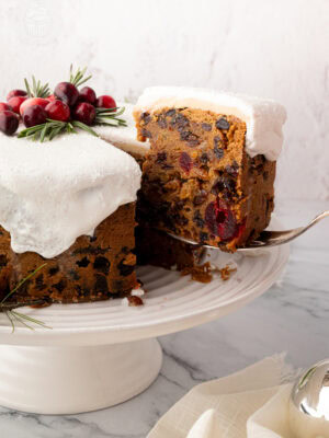 Classic British Christmas cake with a slice being lifted from the cake stand, showing dense fruit cake texture. Traditional UK Christmas cake recipe.