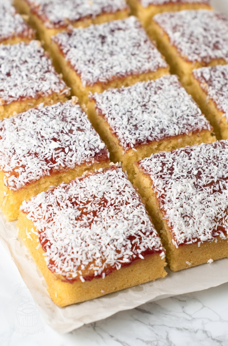 Close-up of a slice of old school cake on baking paper, with golden sponge, vibrant jam, and coconut.
