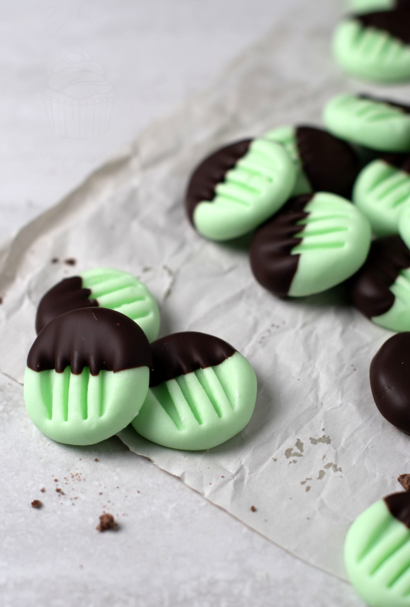Mint green peppermint creams partially dipped in chocolate are arranged on crinkled parchment paper. These peppermint creams boast a ridged pattern achieved by pressing with a fork, adding texture to their smooth surface
