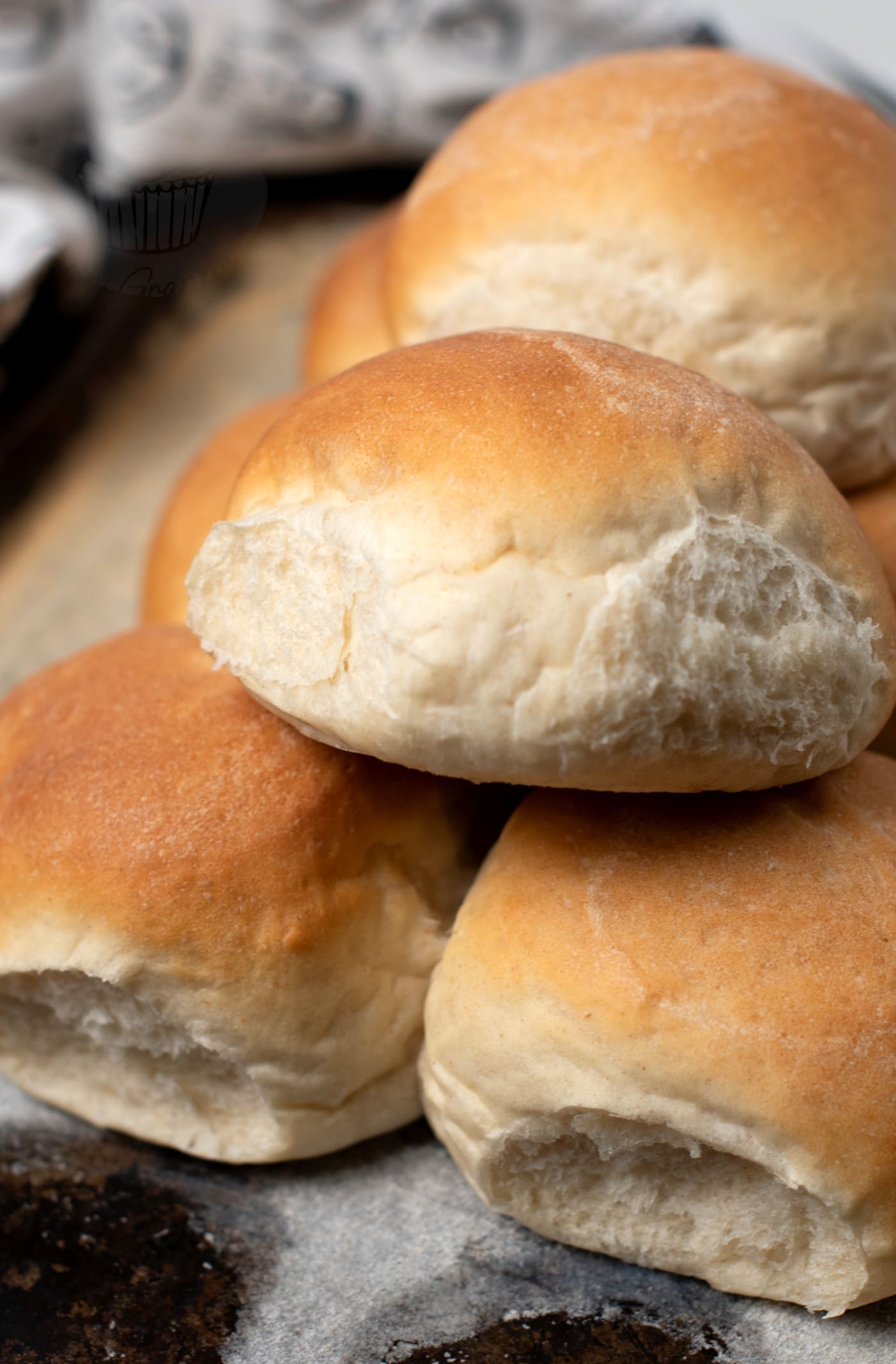 A stack of freshly baked Scottish morning rolls sits on a baking tray. These round delights boast a light golden-brown crust and an irresistibly soft, fluffy texture.