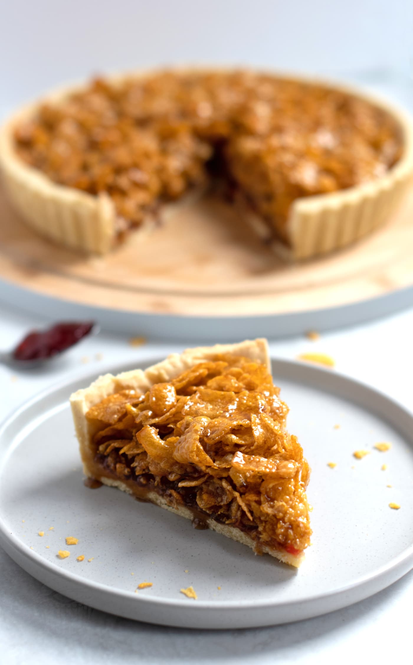 Slice of cornflake tart, on a grey plate, with the rest of the tart on a board behind.