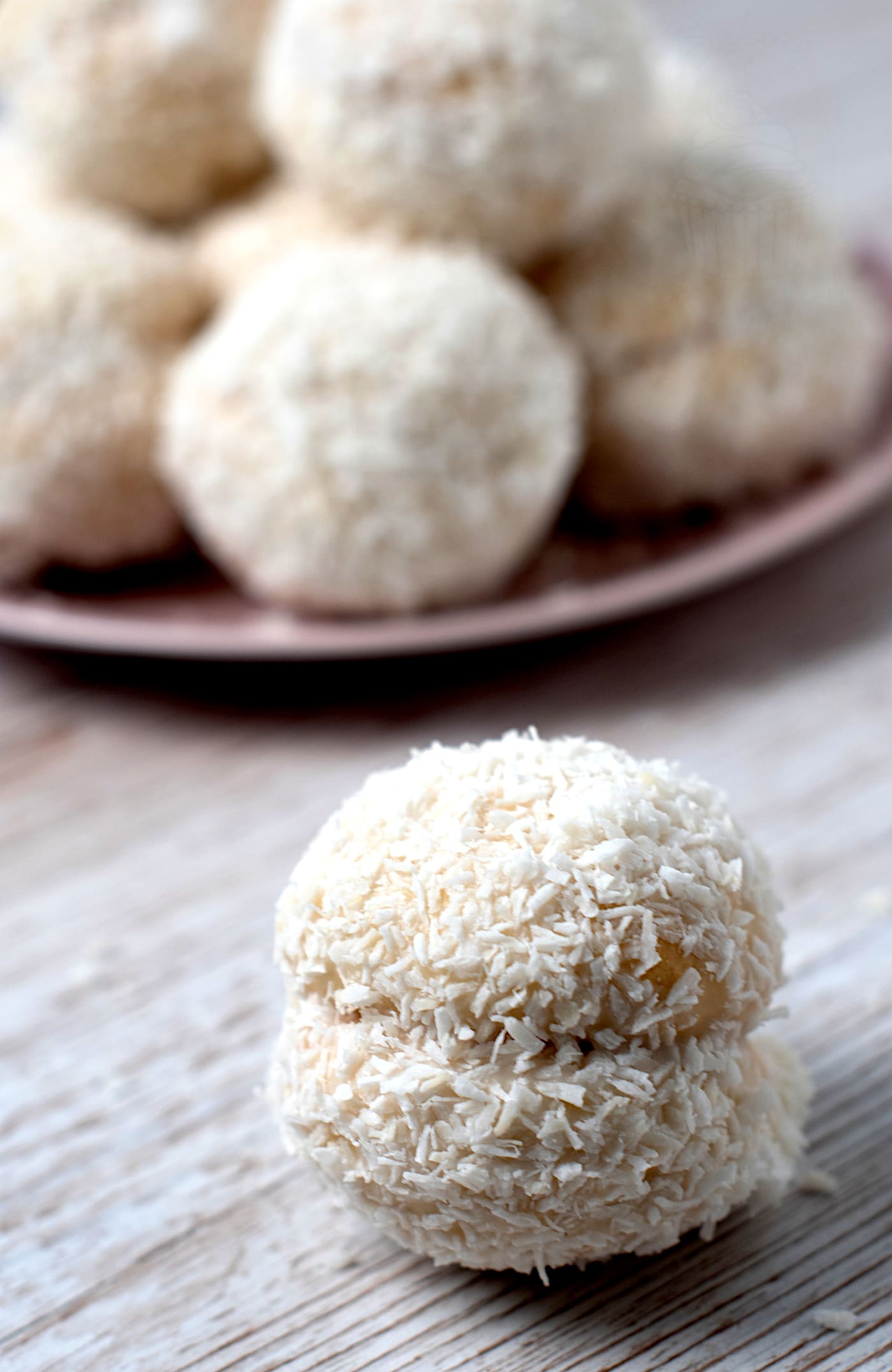 Homemade Scottish Snowball coated in icing and desiccated coconut with more on a plate behind.