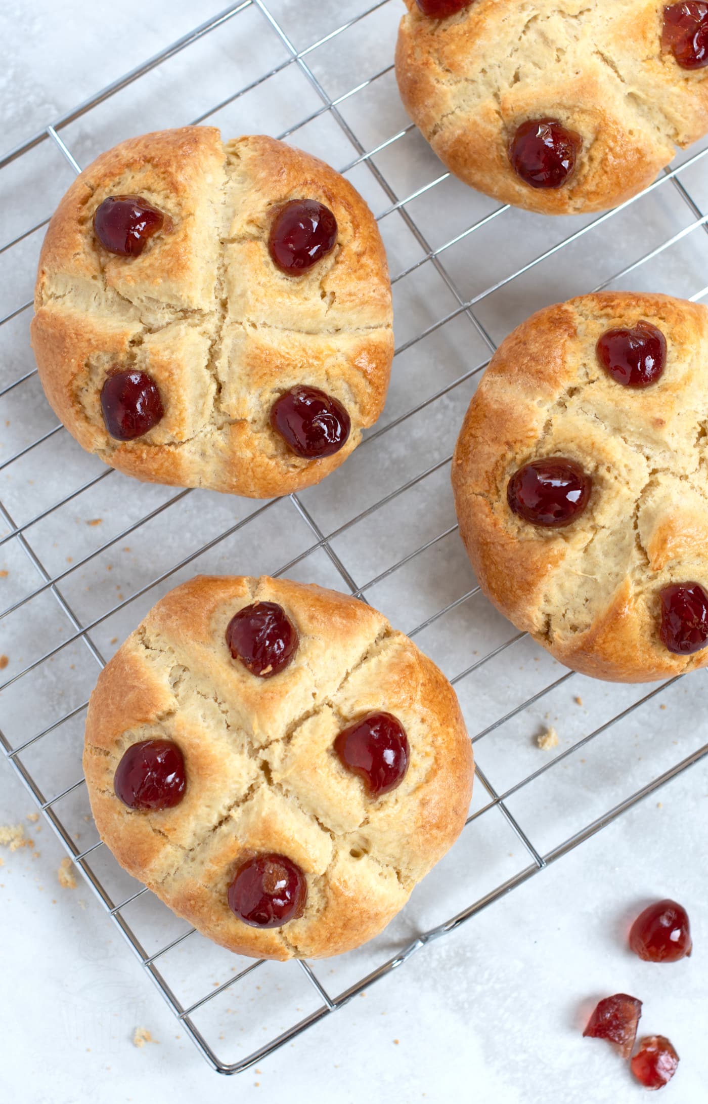 Overhead view of 4 homemade Victoria Scones, on a wire rack, with extra glace cherries scattered around them.