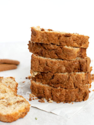 Slices of Banana Biscoff bread, stacked on top of each other, with a couple of extra slices to the side and some Biscoff biscuits in the background.
