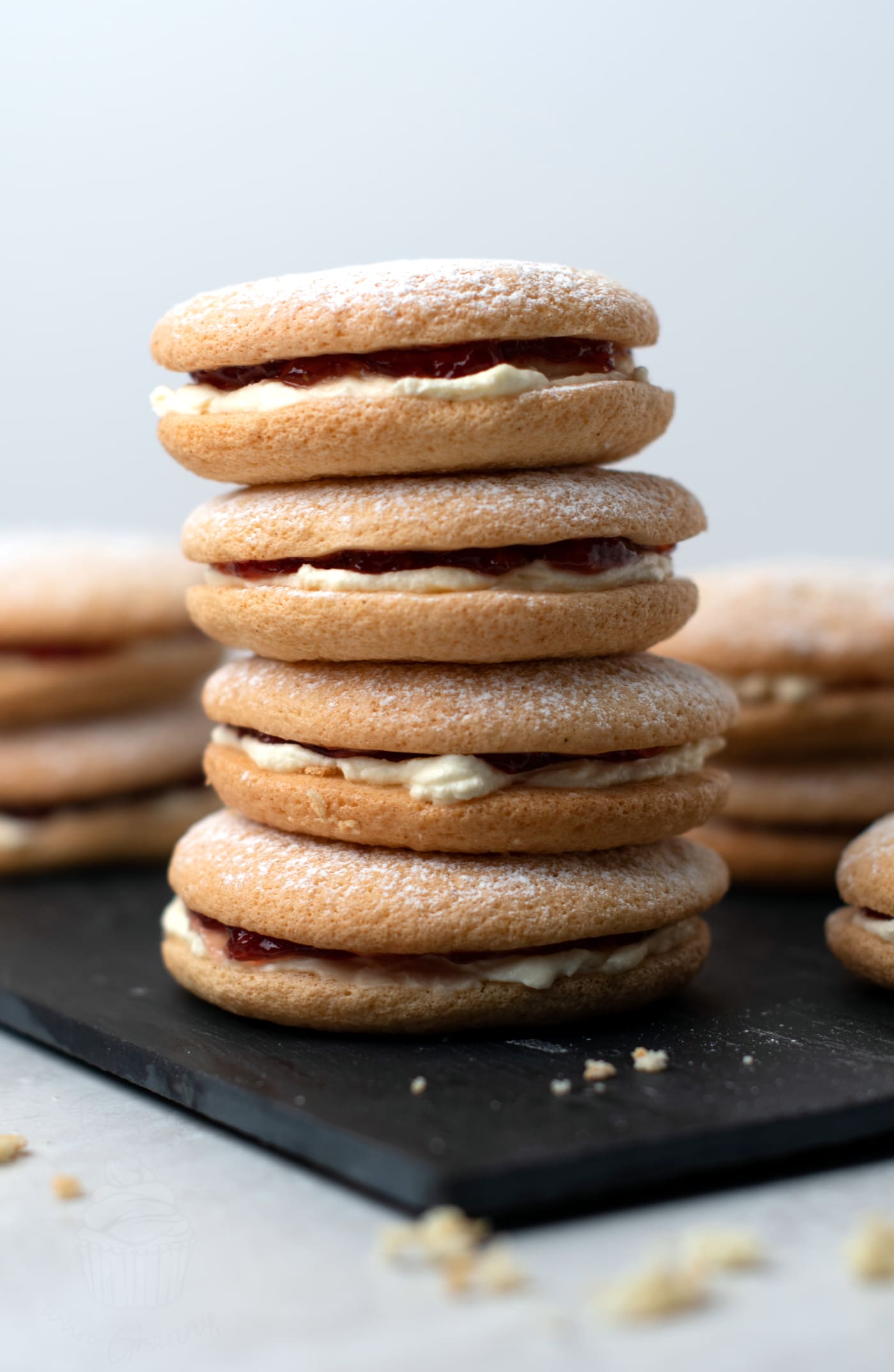A stack of four Sponge Drop cakes. The soft sponge biscuits have cream and jam poking out the edges of them.