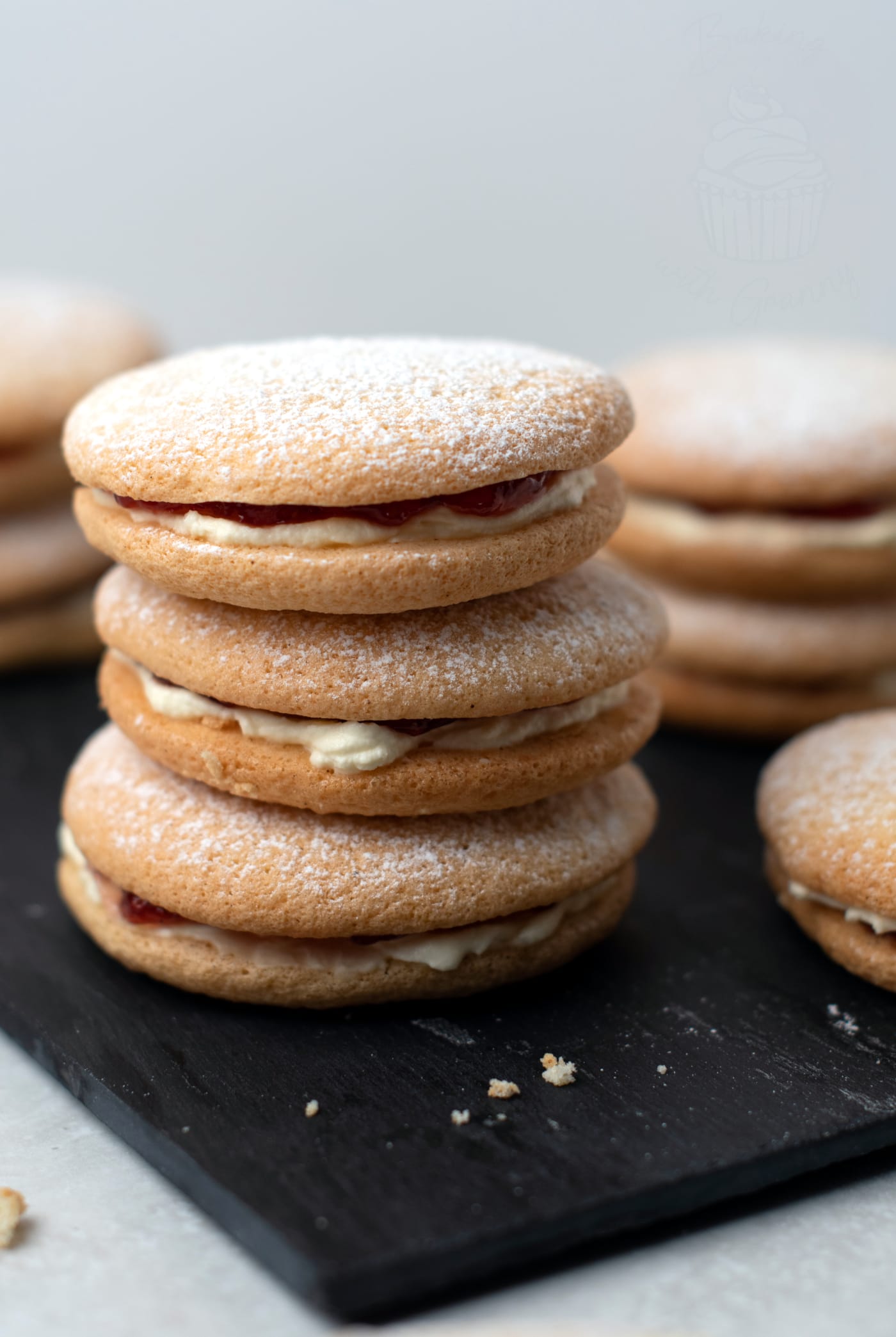 A few Sponge Drops piled on top of each other. The jam and whipped cream filling can be seen and there are some crumbs scattered around.