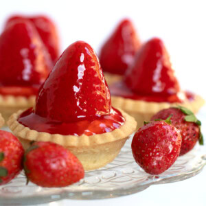 Scottish strawberry tarts, sat on a glass stand, with strawberries placed around.