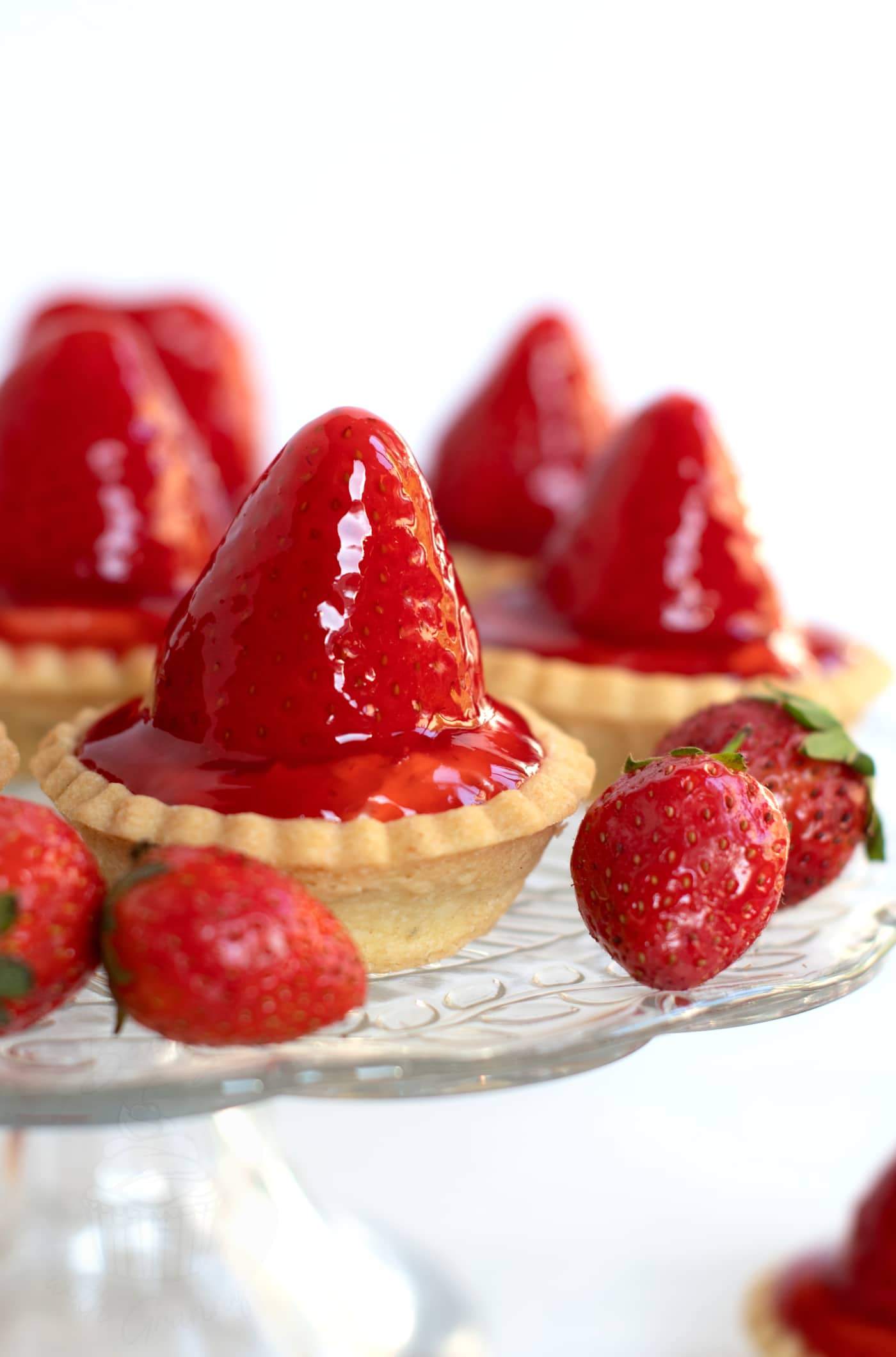 Scottish strawberry tarts, sat on a glass stand, with strawberries placed around.