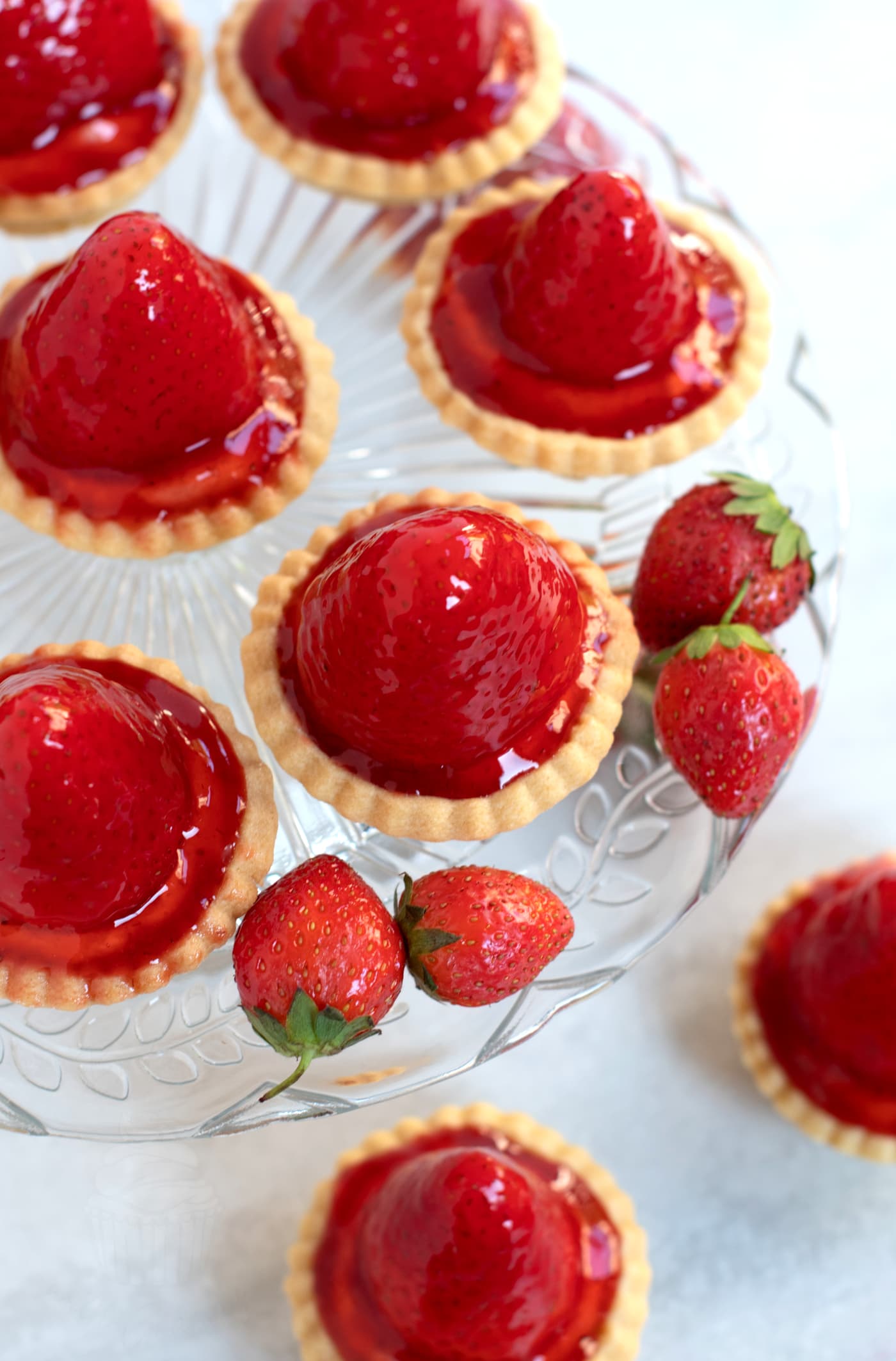 Overhead view of individual strawberry tarts, on top of a glass cake stand, with extra Scottish strawberries placed around.