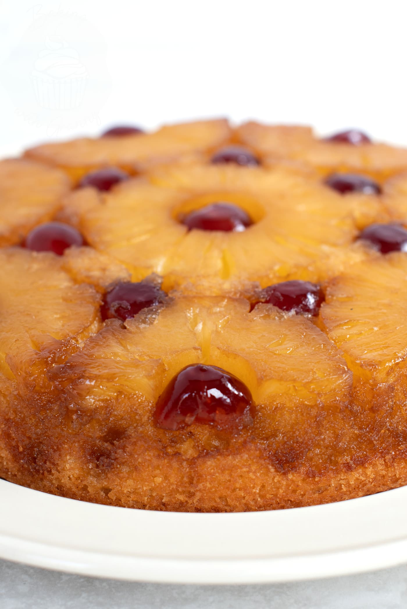 Upside Down Pineapple cake on a light cream plate. The red cherries and golden yellow pineapple rings can be seen on top of the sponge cake bottom.