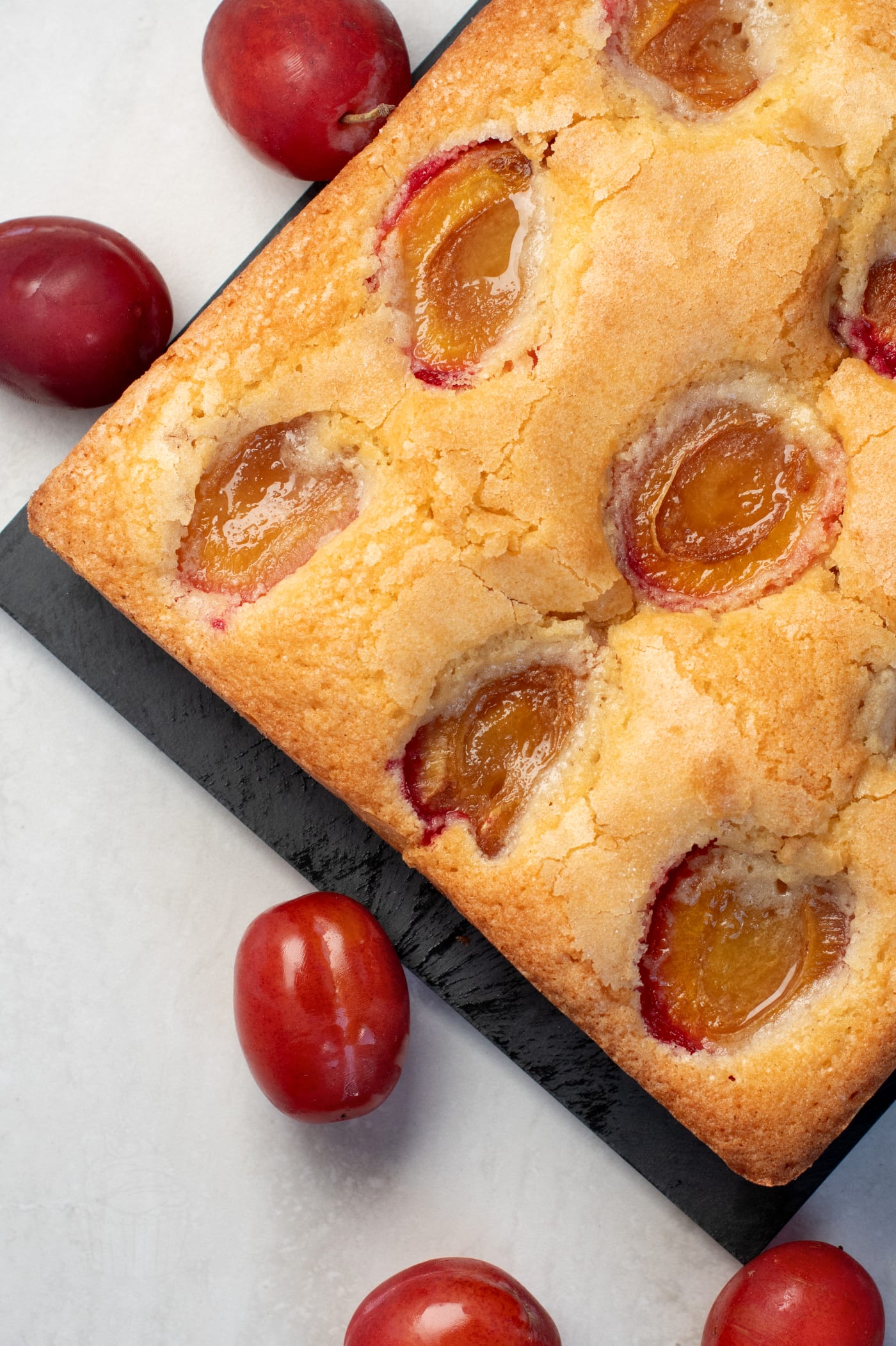 Square plum cake with baked plum halves and whole red plums alongside.