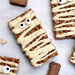 Mummy Mars Bar Slices arranged on greaseproof paper with white chocolate bandages and edible eyes.