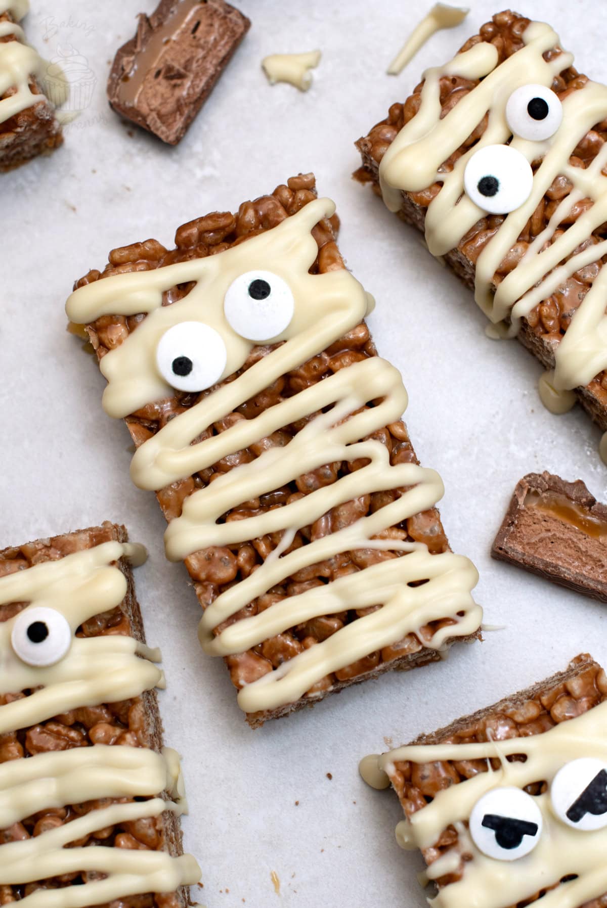 Close-up of Mummy Mars Bar Slices with white chocolate bandages and edible eyes, with Mars Bar pieces on a light surface.